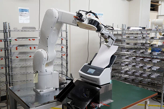 産業用ロボットがスキャナーの原稿台にコピー用紙をセットする様子